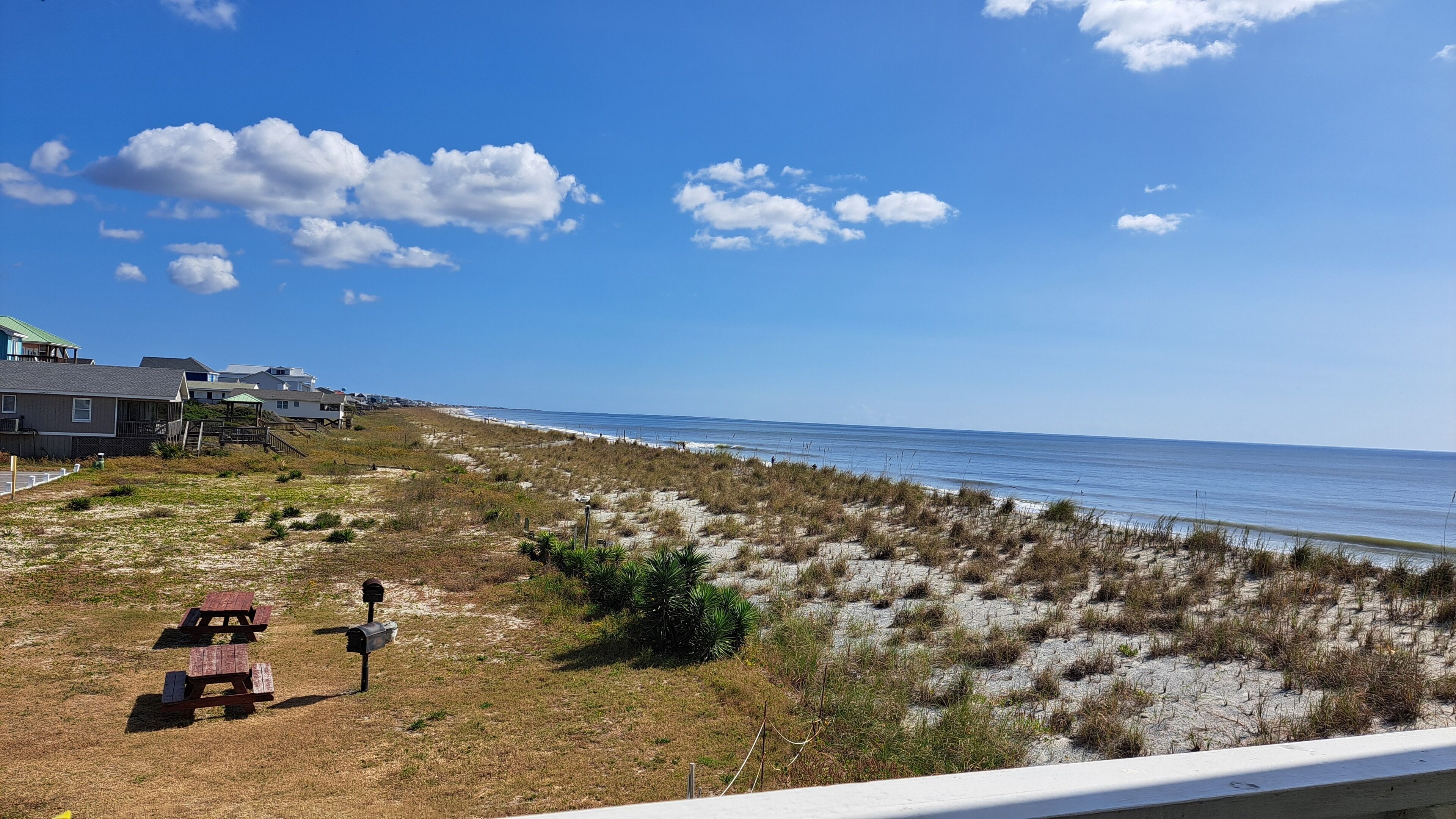 Vista de playa con casas, mesas de picnic y un buzón.