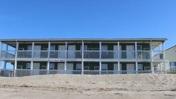 A two-story motel with a balcony on each floor, located on a sandy beach.