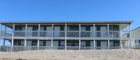A two-story motel with a balcony on each floor, located on a sandy beach.