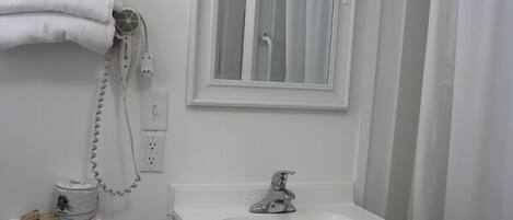 Une salle de bain avec un lavabo, un miroir et des toilettes, le tout de couleur blanche.