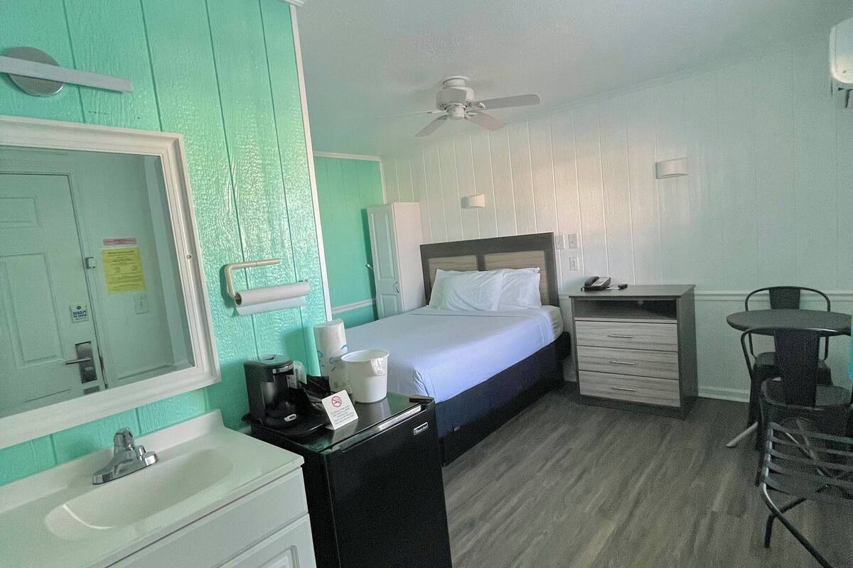 Una habitación de hotel con cama, escritorio, silla, lavamanos y espejo.