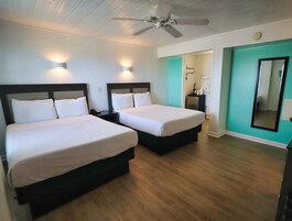 Quarto de hotel com duas camas, um ventilador de teto, banheiro visível através de uma porta aberta e um espelho na parede.