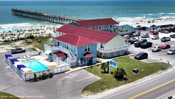 Un motel con piscina, un muelle al fondo y una playa a lo lejos.