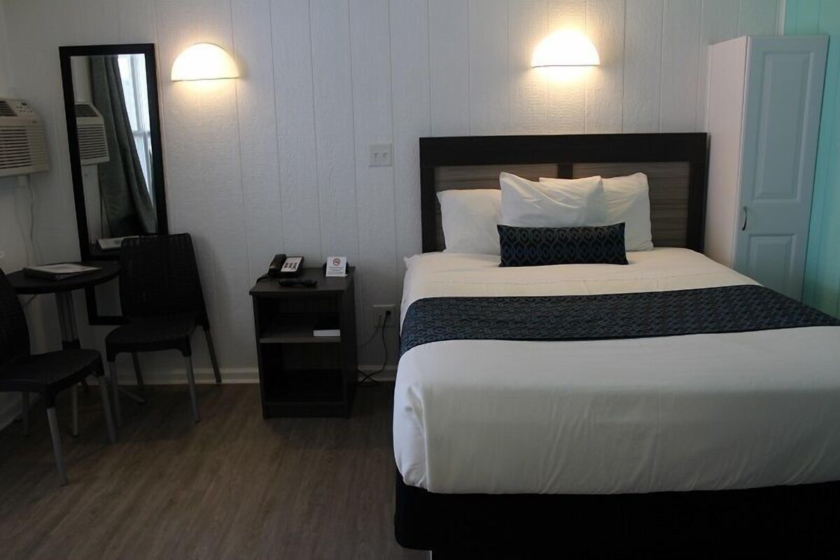 A hotel room with a bed, a desk, a chair, a mirror, and a wardrobe.