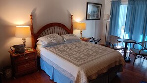 A neatly arranged bedroom with a large bed, two bedside tables with lamps, a chair, and a small table. - Comfy Corner a large comfortable  one room condo with a strict no smoking policy (Fairfield Harbour, New Bern)