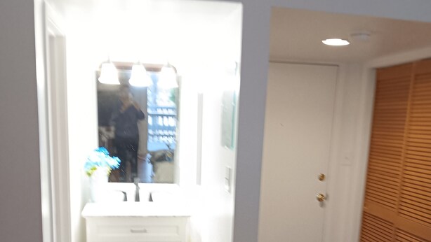 A narrow hallway with a white vanity and mirror, wooden flooring, and a door with a louvered design. - Comfy Corner a large comfortable  one room condo with a strict no smoking policy (Fairfield Harbour, New Bern)