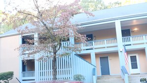 A two-story building with a balcony on the second floor, a flag, and a car parked in front. - Comfy Corner a large comfortable  one room condo with a strict no smoking policy (Fairfield Harbour, New Bern)