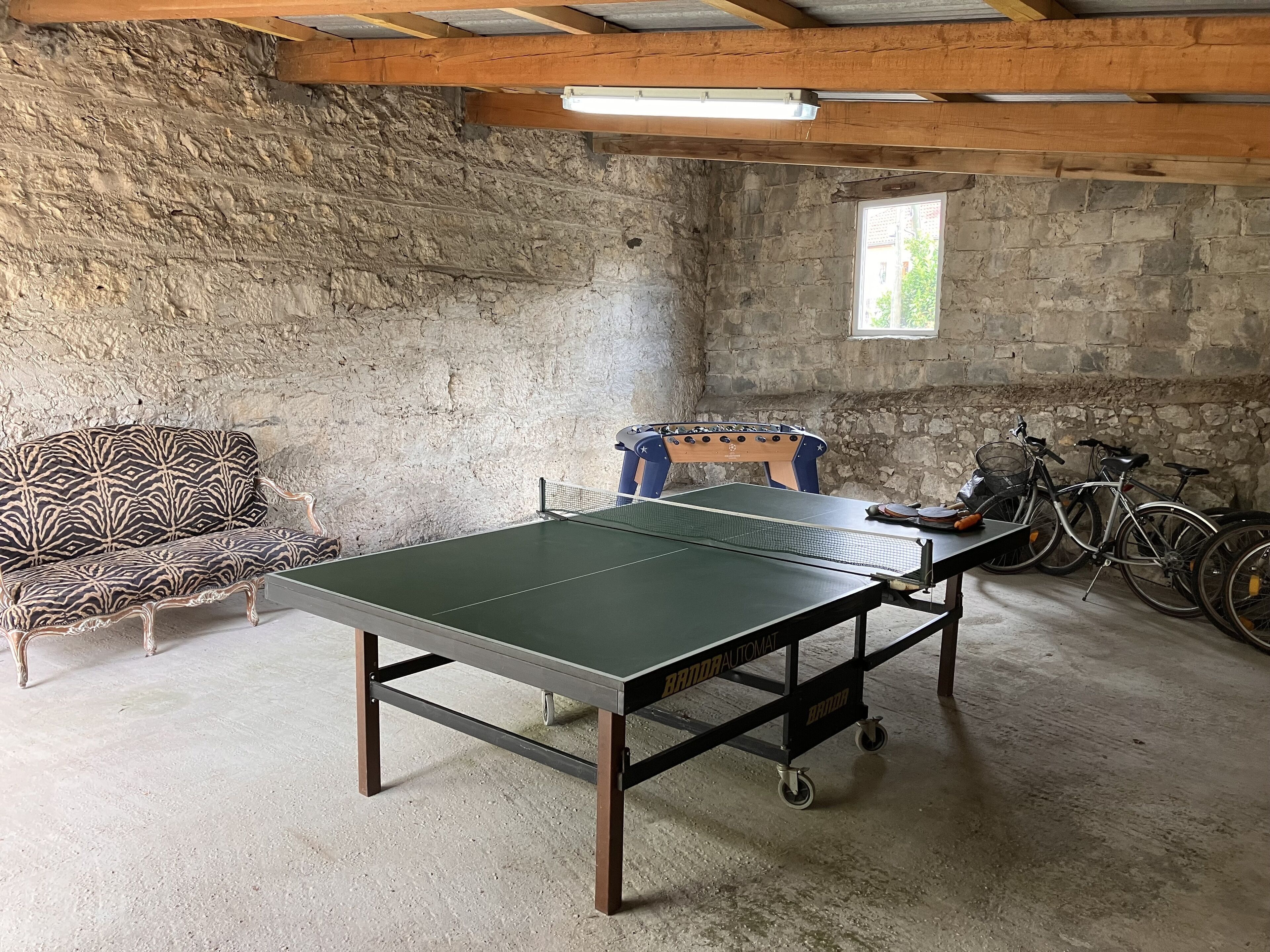 Una habitación con mesa de ping pong, sofá, silla y bicicletas.