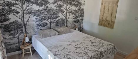 A bedroom with a bed, a nightstand, a wall tapestry, and a hanging tapestry.