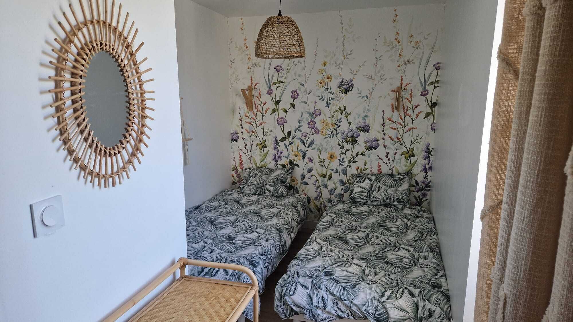 A small bedroom with two single beds, a woven mirror, and a hanging light fixture.