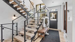 A modern staircase with glass railings and wooden steps, leading to a room with a dark door and a bench. - Abode at Hollow Mountain, private hot tub, sound system, garden (Park City)