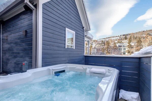 Een hottub in een houten chalet met uitzicht op een besneeuwde heuvel.
