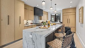 A modern kitchen with wooden cabinets, a marble island, pendant lights, and a black chair. - Abode at Hollow Mountain, private hot tub, sound system, garden (Park City)