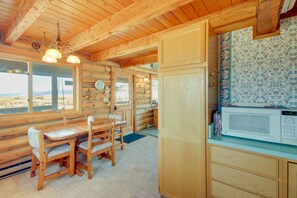 Ein Holzblockhaus Innenansicht mit Essbereich, einer Küche inklusive Mikrowelle und Blick durch das Fenster.