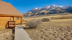 Une cabane en bois dotée d’un porche et offrant une vue dégagée sur des montagnes enneigées en arrière-plan.