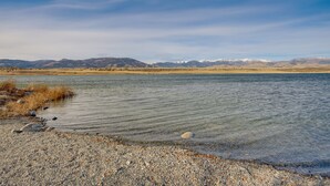 Un lac paisible, bordé d’une plage de galets, avec des montagnes lointaines se découpant sur un ciel dégagé.