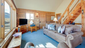 L’intérieur d’une cabane en rondins, avec un canapé, un téléviseur et un escalier en bois.