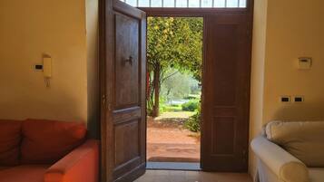 Una stanza con una porta in legno che dà su un giardino, un divano rosso e un divano color beige.