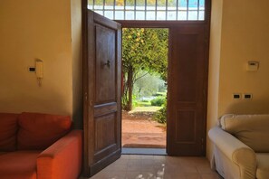 Une pièce avec une porte en bois donnant sur un jardin, un canapé rouge et un canapé beige.
