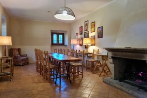 Een eetruimte met een lange houten tafel, omringd door stoelen, een open haard en wandlampen.