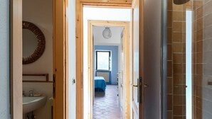 Un couloir mène à une chambre qui comprend un lit, une fenêtre et une salle de bain avec un lavabo.