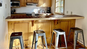 A kitchen with wooden cabinets, a stainless steel microwave, a gas stove, and a large window. There are three metal stools in front of the counter. - Cozy Ski-in Ski-out Snowbird Townhouse (Alta)