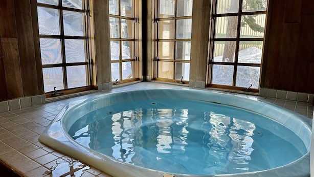 A hot tub with a tiled floor and wooden walls, surrounded by windows with a view of a snowy landscape. - Cozy Ski-in Ski-out Snowbird Townhouse (Alta)