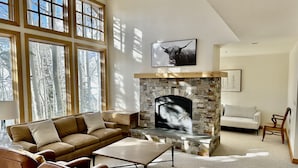 A living room with a stone fireplace, large windows, a sofa, and a coffee table. - Cozy Ski-in Ski-out Snowbird Townhouse (Alta)