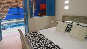 Un dormitori amb llit, una tauleta de nit, un mirall i vista a una piscina per una porta oberta.