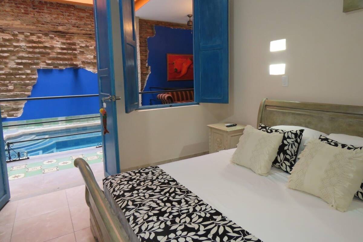 A bedroom with a bed, a nightstand, a mirror, and a view of a pool through an open door.