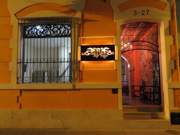 Entrada de hotel con una reja de hierro forjado, un letrero de neón y un arco de piedra.