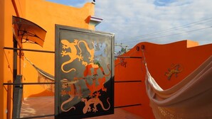 Una cadira de corda penjada entre dues parets taronja amb un mural negre i taronja que representa llangostes.