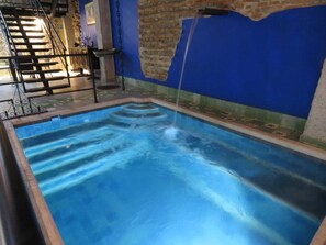 Una piscina con una fuente de agua, una escalera y un muro de ladrillo.