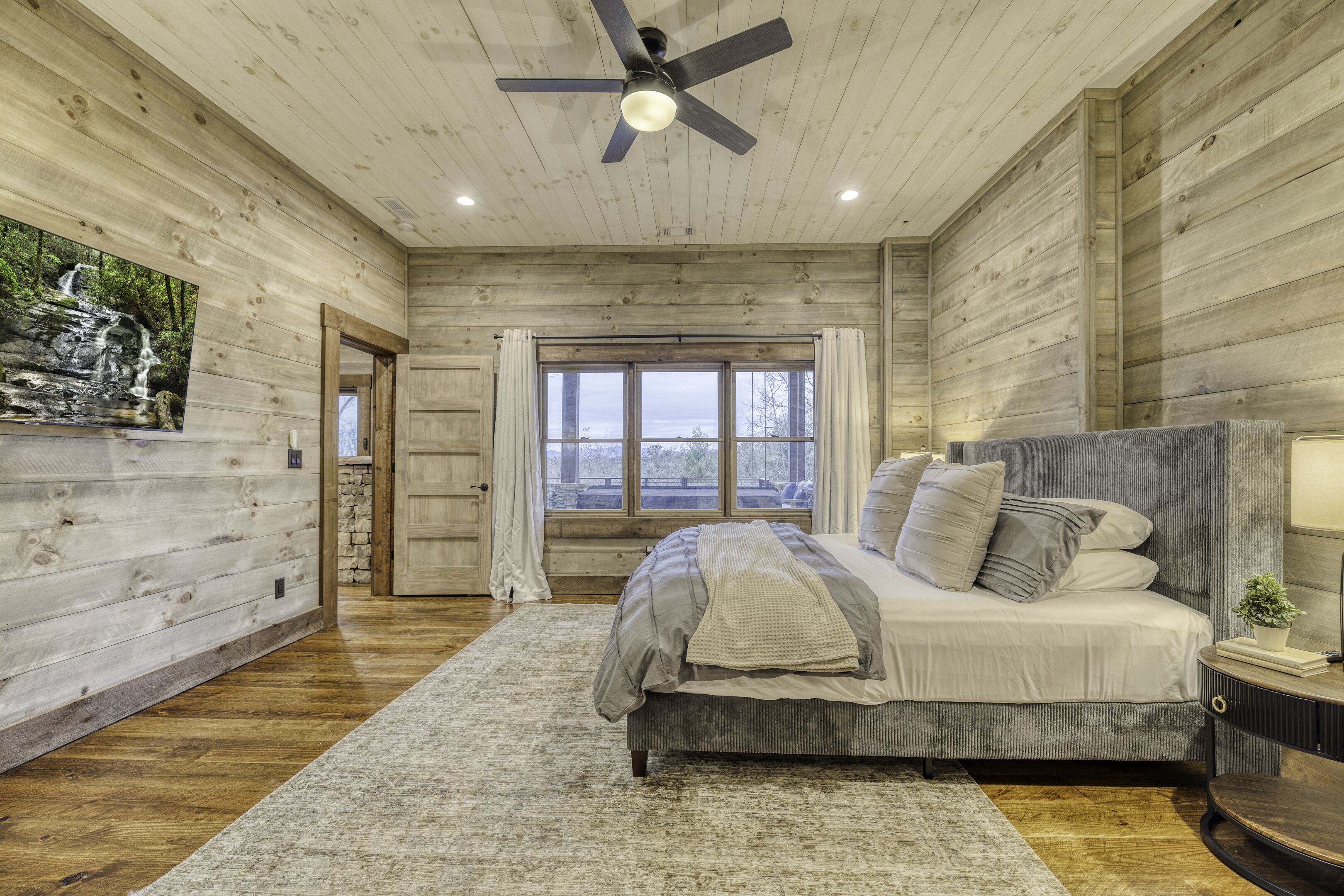 A bedroom with a bed, a ceiling fan, a window, and a view of the outdoors.