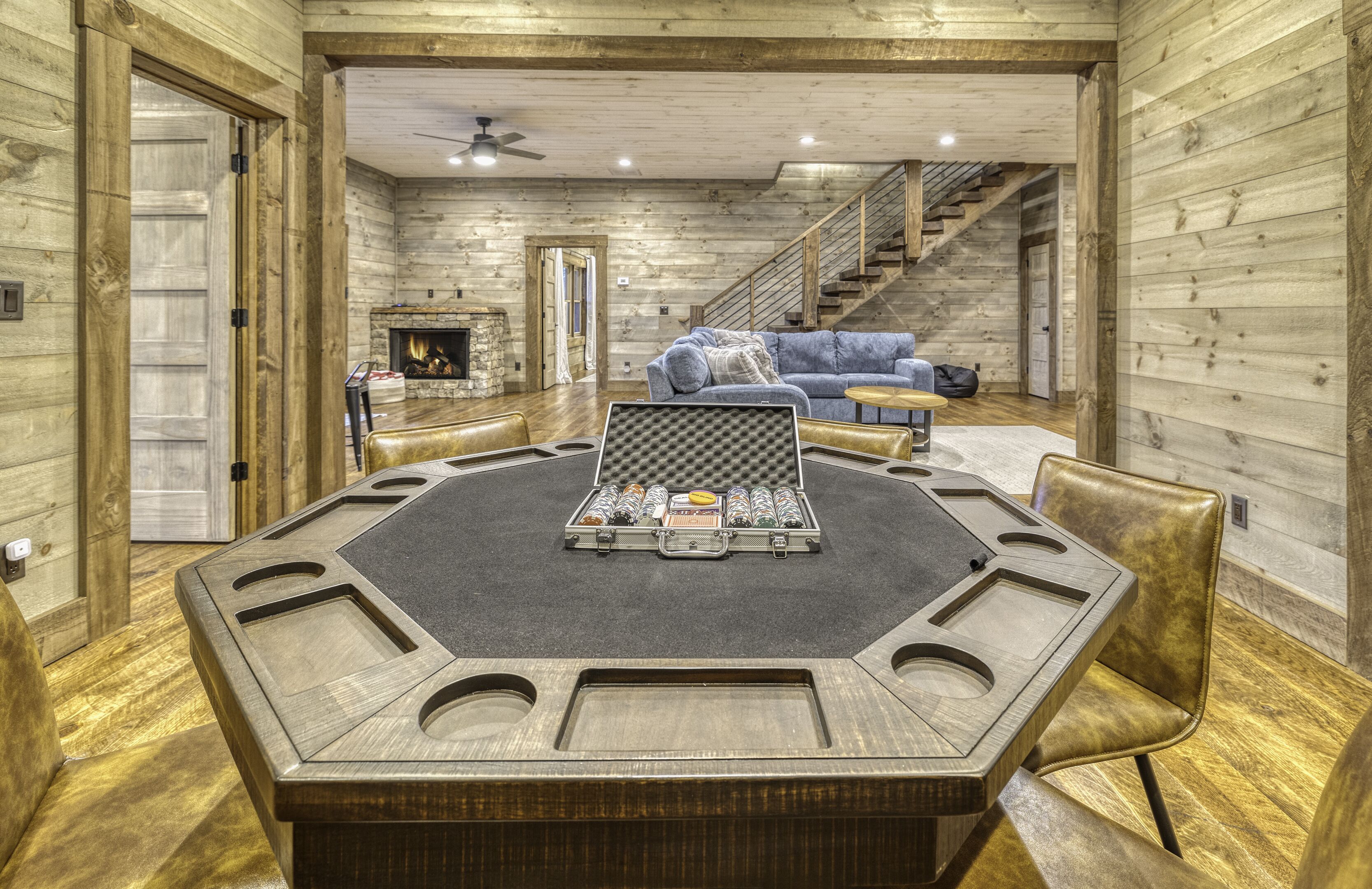 A spacious room with a large wooden table, leather chairs, a blue sofa, and a staircase.
