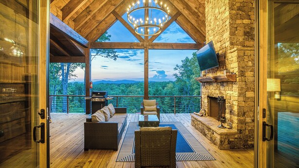 Eine Holzdar Terrasse mit Kamin aus Stein, einem großen Kronleuchter und Blick auf die Berge.