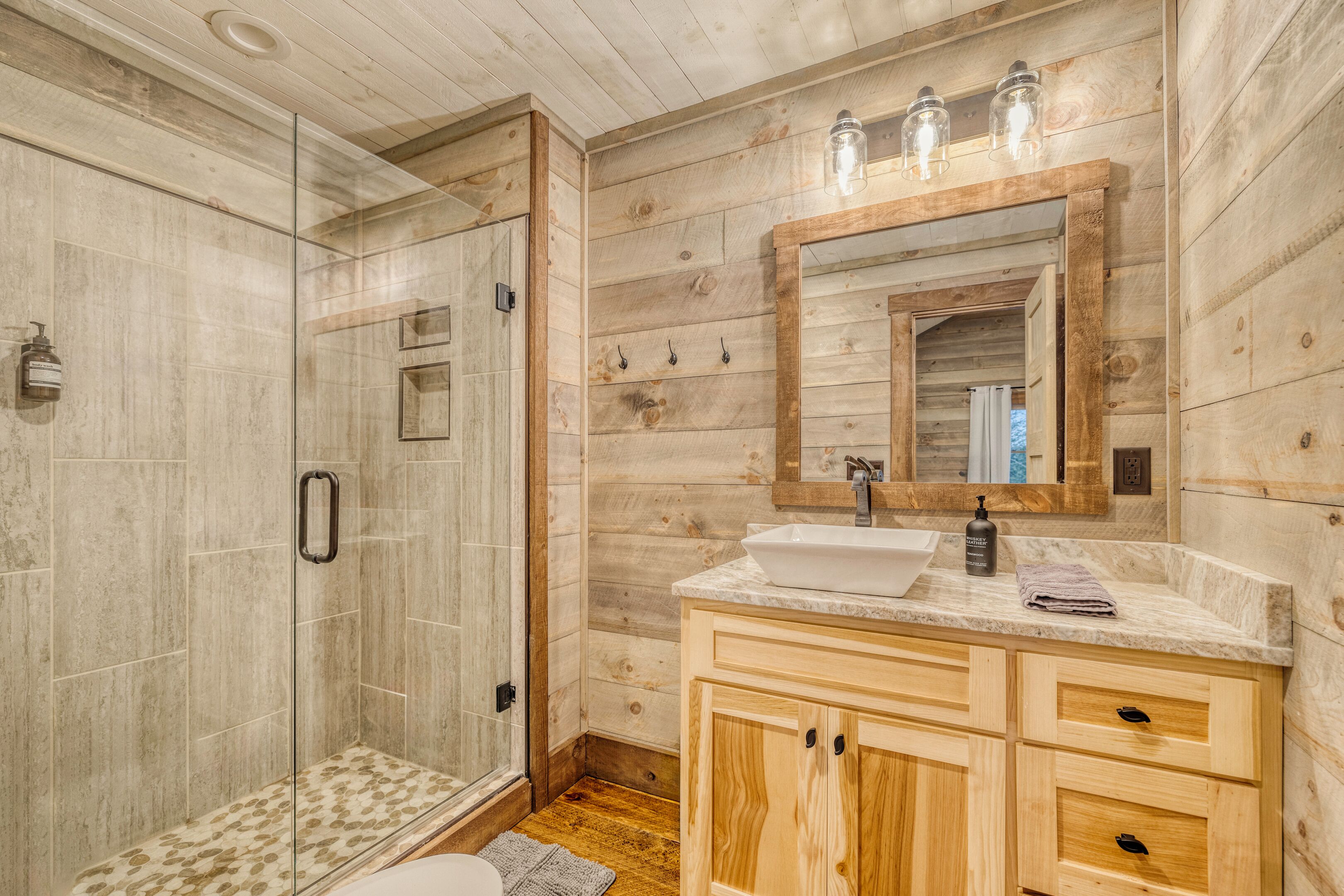 A bathroom with a glass-enclosed shower, a wooden vanity with a sink, and a mirror above the vanity.