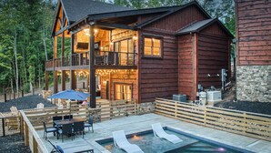 Eine zweistöckige Holzhütte mit Pool, Sitzgelegenheiten im Freien und einem Kamin aus Stein.