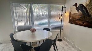 Un comedor con una mesa redonda, seis sillas, un florero con flores, una lámpara de pie y un cuadro colgado en la pared.