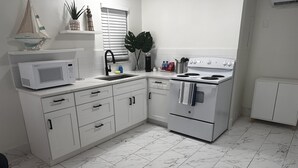 Una cocina con armarios blancos, microondas, estufa y lavaplatos.