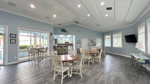 A spacious dining area with a large wooden table and chairs, a kitchen in the background, and a TV mounted on the wall. - Seashell Escape (New Smyrna Beach)