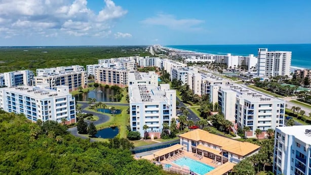 A coastal resort with multiple high-rise buildings, a central pool, and a view of the ocean. - Seashell Escape (New Smyrna Beach)