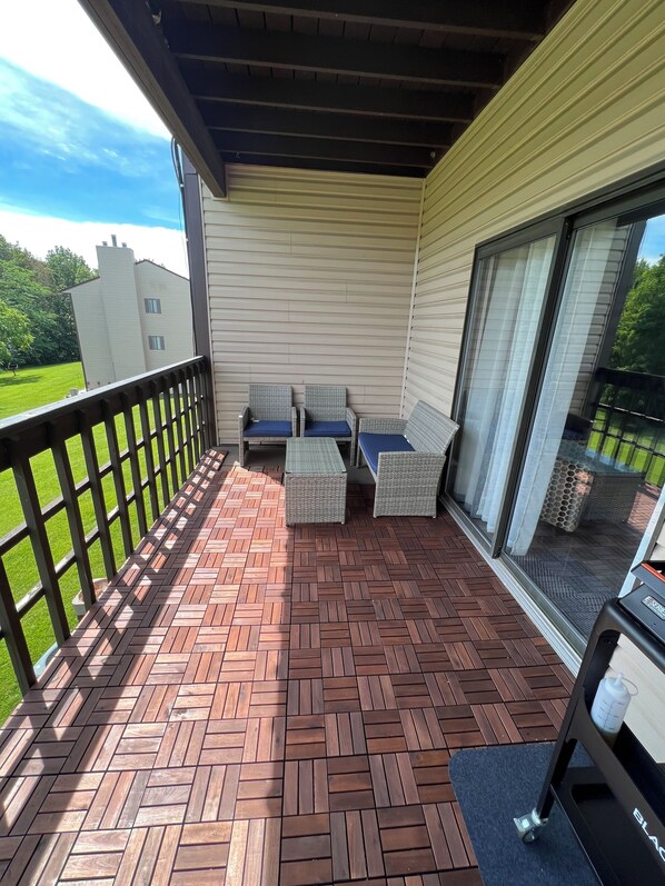 Un patio cubierto con suelo de madera en patrón de espiga, mobiliario de mimbre y un gran ventanal corredera.