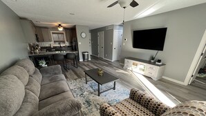 Una sala de estar moderna con un sofá modular, un sillón estampado, una mesa de centro y un televisor de pantalla plana montado en la pared.
