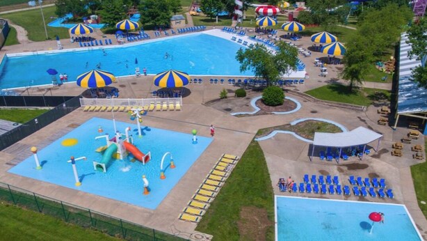 Una amplia piscina al aire libre con varias pistas, rodeada de sombrillas, sillas de descanso y una zona de juegos acuáticos.