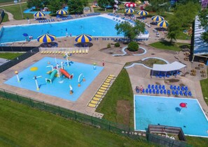 Una amplia piscina al aire libre con varias pistas, rodeada de sombrillas, sillas de descanso y una zona de juegos acuáticos.