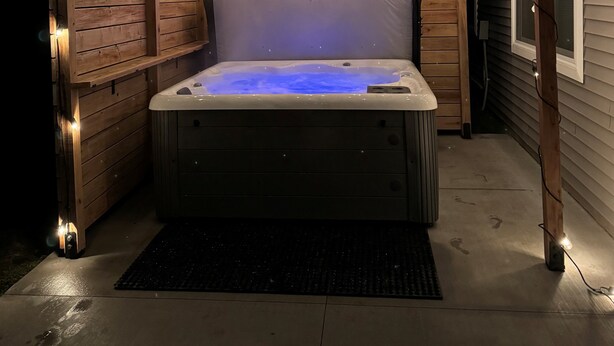 Een hottub onder een houten pergola met lichtslingers, omgeven door houten wanden.