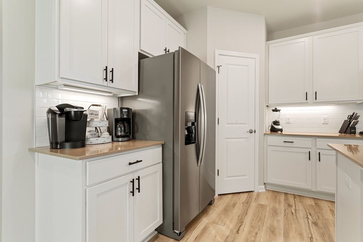 A modern kitchen with white cabinets, a stainless steel refrigerator, a coffee maker, and a blender.