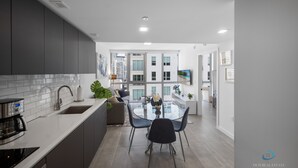 A modern kitchen with a central island, a dining area with a glass table, and a view of high-rise buildings. - Apartment at Downtown Miami (Miami)