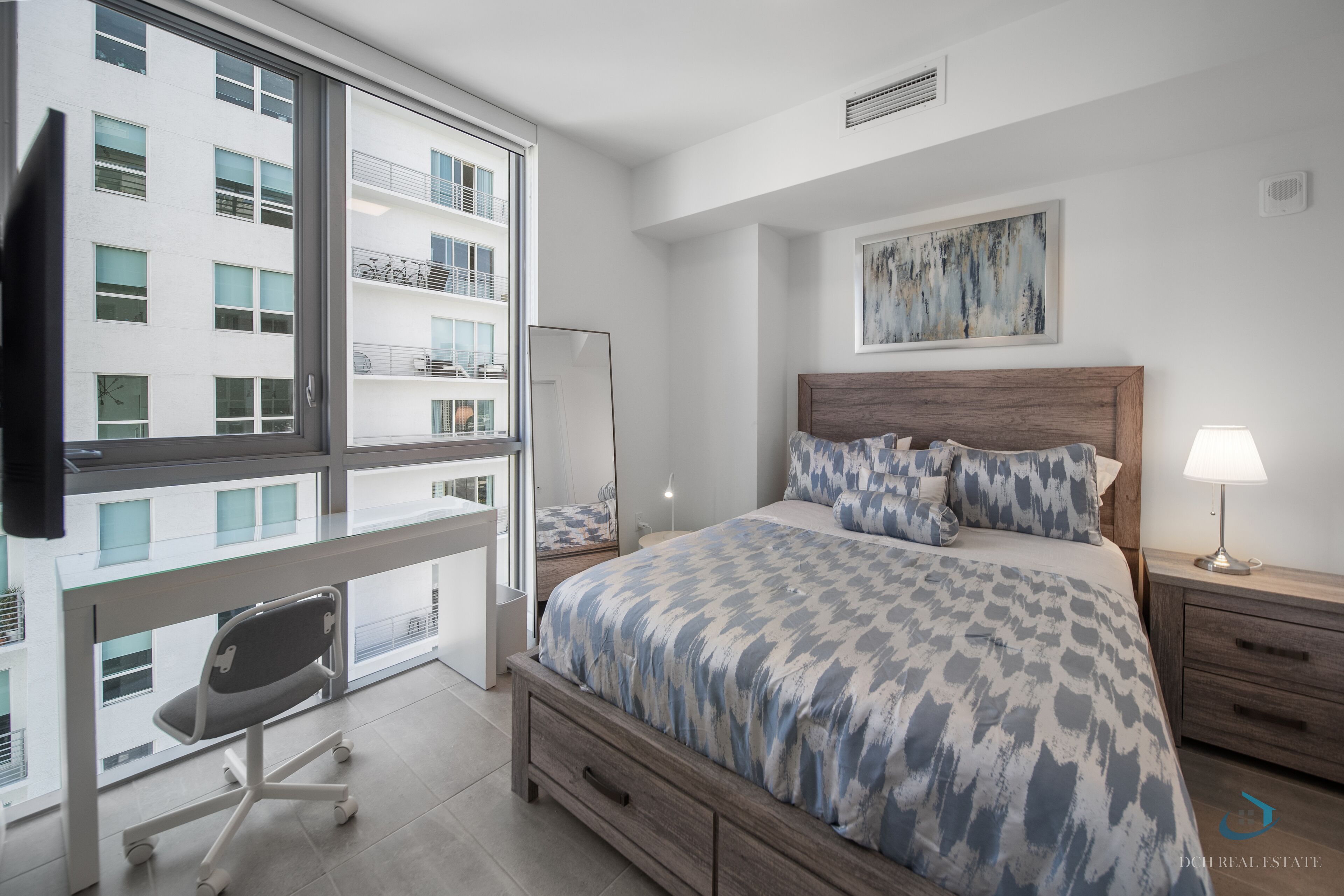 Une chambre avec un grand lit, un bureau et une fenêtre donnant sur un immeuble.